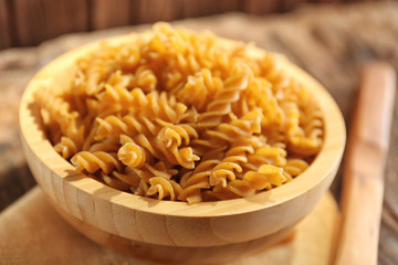 Raw pasta in bowl on wooden table closeup