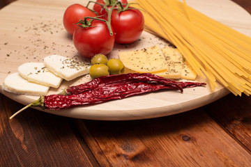 Cooking Italian pasta spaghetti. On a wooden Board are the ingredients for pasta: tomatoes, cheese, basilic, olives.