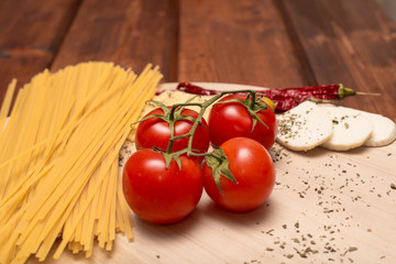 Cooking Italian pasta spaghetti. On a wooden Board are the ingredients for pasta: tomatoes, cheese, basilic, olives.