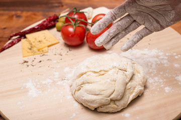 Female hands make a pizza dough. On a wooden Board are the ingredients for the pizza: tomatoes, cheese, basilic, olives.