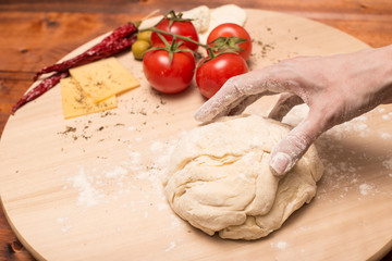 Female hands make a pizza dough. On a wooden Board are the ingredients for the pizza: tomatoes, cheese, basilic, olives.