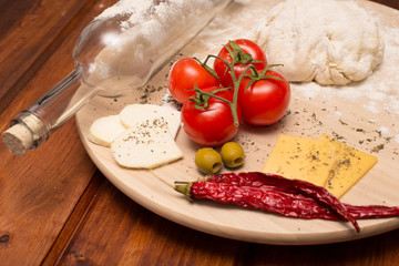 The preparation of pizza dough. On a wooden Board rolling pin is a bottle of wine and ingredients for pizza: tomatoes, cheese, basilic, olives.