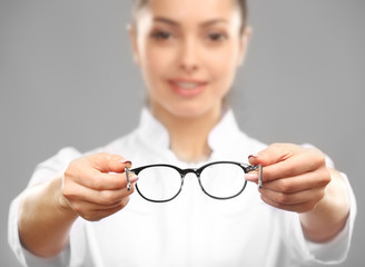 Young female doctor giving glasses on grey background