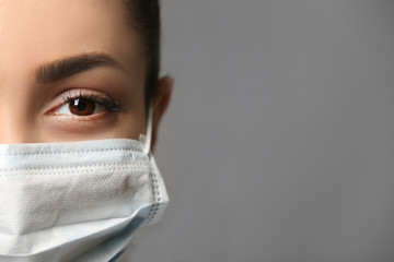 Young female doctor in medical mask on grey background
