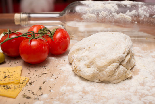 The preparation of pizza dough. On a wooden Board rolling pin is a bottle of wine and ingredients for pizza: tomatoes, cheese, basilic, olives.