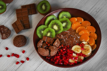 Bowl with chocolate cookies, sliced fruits, chia and pomegranate seeds on wooden table