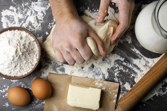 Male hands kneading raw dough on kitchen table