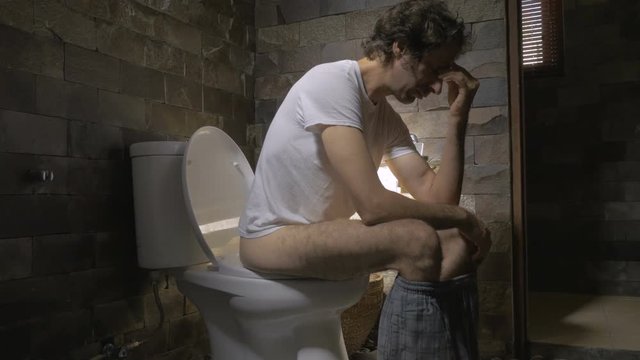 Dolly shot of a man sitting on a toilet feeling ill, depressed, or upset