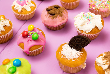 Multiple muffins decorated with multicolored frosting, cocoa powder and beans, candies and whipped cream top view toned selective focus close up