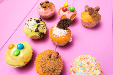Multiple muffins decorated with multicolored frosting, cocoa powder and beans, candies and whipped cream top view toned selective focus