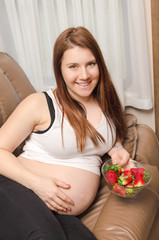 Obraz na płótnie Canvas pregnant woman lying in the sofa and hold plate with strawberry