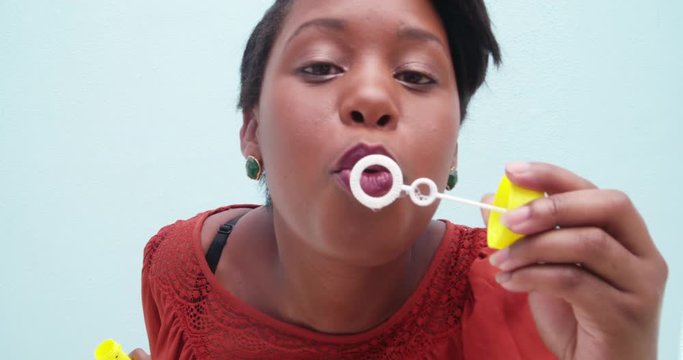 Childish young african woman blowing bubbles