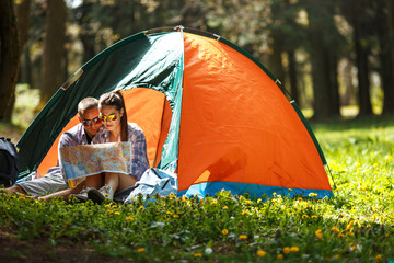 Couple camping. Young couple sitting in front of the tent and examining the map.