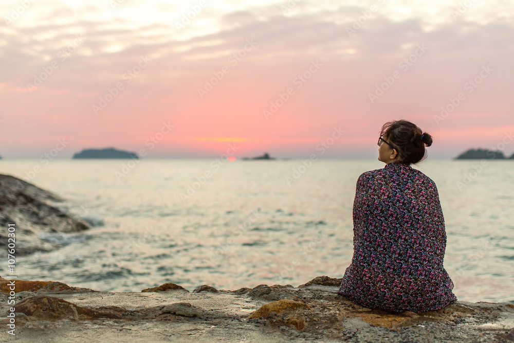 Wall mural lonely woman sitting on the seashore after sundown.