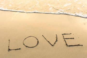 Love - written manually on the texture of sea sand.