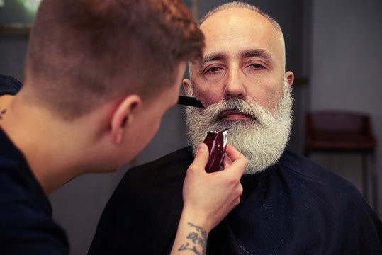 Barber making haircut to handsome attractive senior man with bea