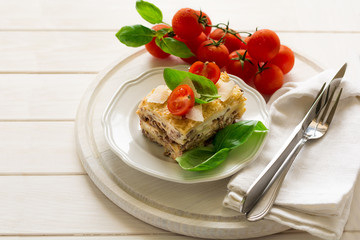 Homemade lasagna with bechamel sauce decorated basil leaves and cherry tomatoes on white plate