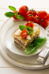 Homemade lasagna with bechamel sauce decorated basil leaves and cherry tomatoes on white plate