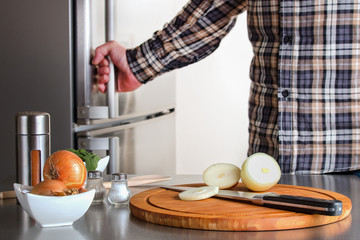 Obraz na płótnie Canvas Zwiebeln, Gewürze und Kochzubehör vor einem Kühlschrank der von einem Mann geöffnet wird