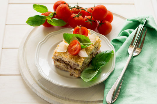 Homemade lasagna with bechamel sauce decorated basil leaves and cherry tomatoes on white plate