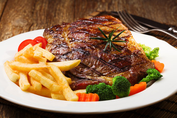 Grilled beef steak served with French fries and vegetables on a