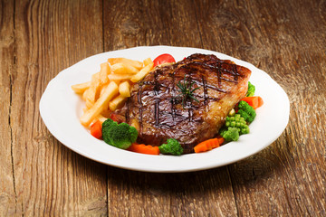 Grilled beef steak served with French fries and vegetables on a