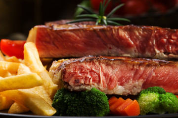 Grilled beef steak served with French fries and vegetables on a