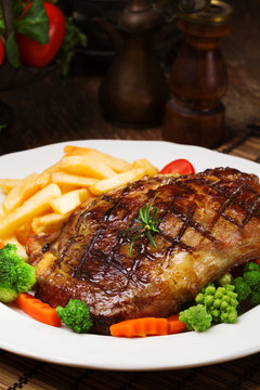 Grilled beef steak served with French fries and vegetables on a