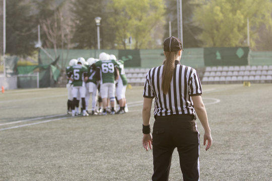 Female American football referee standing on the field and blurred players in the background 