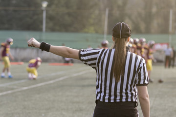 Female American football referee giving signals and blurred players in the background