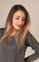 portrait of a cute long-haired young woman in a grey knitted sweater elbow bent looking aside from camera downwards slightly smiling