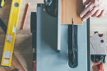 Carpenter cuts wooden board on circular saw wood cutting machine .