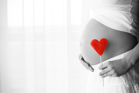 Black and white picture of pregnant woman holding heart sign to one side