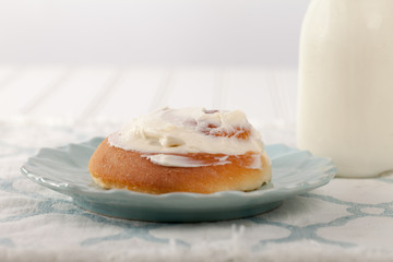 Freshly baked homemade cinnamon roll with cream cheese buttercream frosting and an antique bottle of milk side view