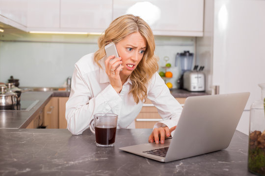 Worried woman in kitchen working on computer