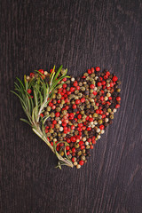 a mixture of peppers ( red, white, black ) in the form of heart with a sprig of rosemary on a black background