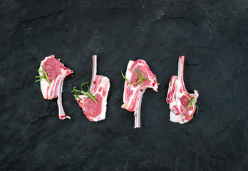 Raw lamb chops. Rack of Lamb with rosemary and spices over black slate stone background.