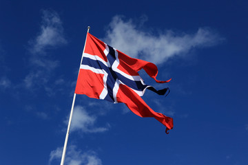 A Norwegian flag blowing in the wind against blue sky with cloud