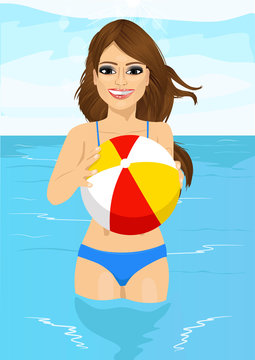 attractive woman holding an inflatable striped ball standing in water