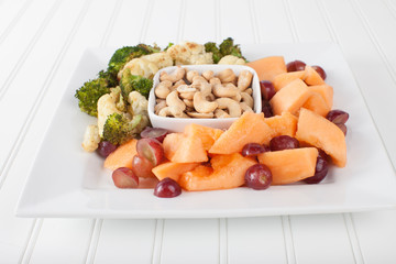 Macro shot of a platter of cashews, cantaloupe, grapes, roasted broccoli, and cauliflower