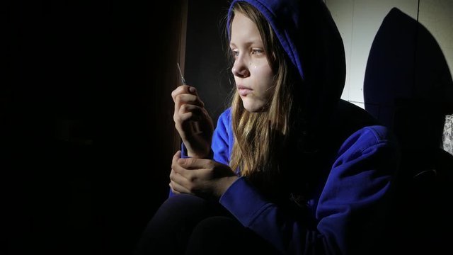 Addicted junkie teen girl with a syringe sitting on a floor and thinking about something. 4K UHD.