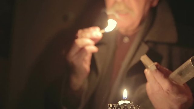 Grandpa lights a candle in a dark room
