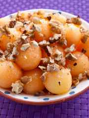 Fruit salad made of sweet melon balls topped with cracked walnuts. Shot over purple background