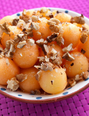 Fruit salad made of sweet melon balls topped with cracked walnuts. Shot over pink background