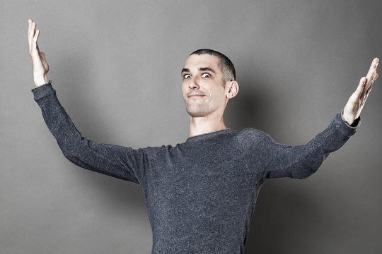 exaggeration concept -  expressive young man with eyes wide open opening his arms wide for theater play or lyric show off, grey background studio