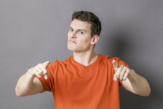 guilt concept - bossy young sporty man accusing or threatening someone with his hands for blame, grey background