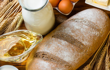 Compisition of diary products - bread, milk, yogurt, eggs, butter, oil and wheat spike on wooden dark background