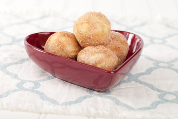 heart shaped bowl filled with mini French breakfast puffs homemade on a blue and white place mat