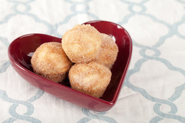 side view of a heart shaped bowl filled with mini French breakfast puffs homemade on a blue and white placemat