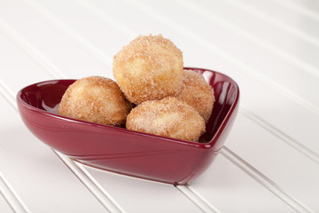 Side view of a heart shaped bowl filled with mini French breakfast puffs on white wood